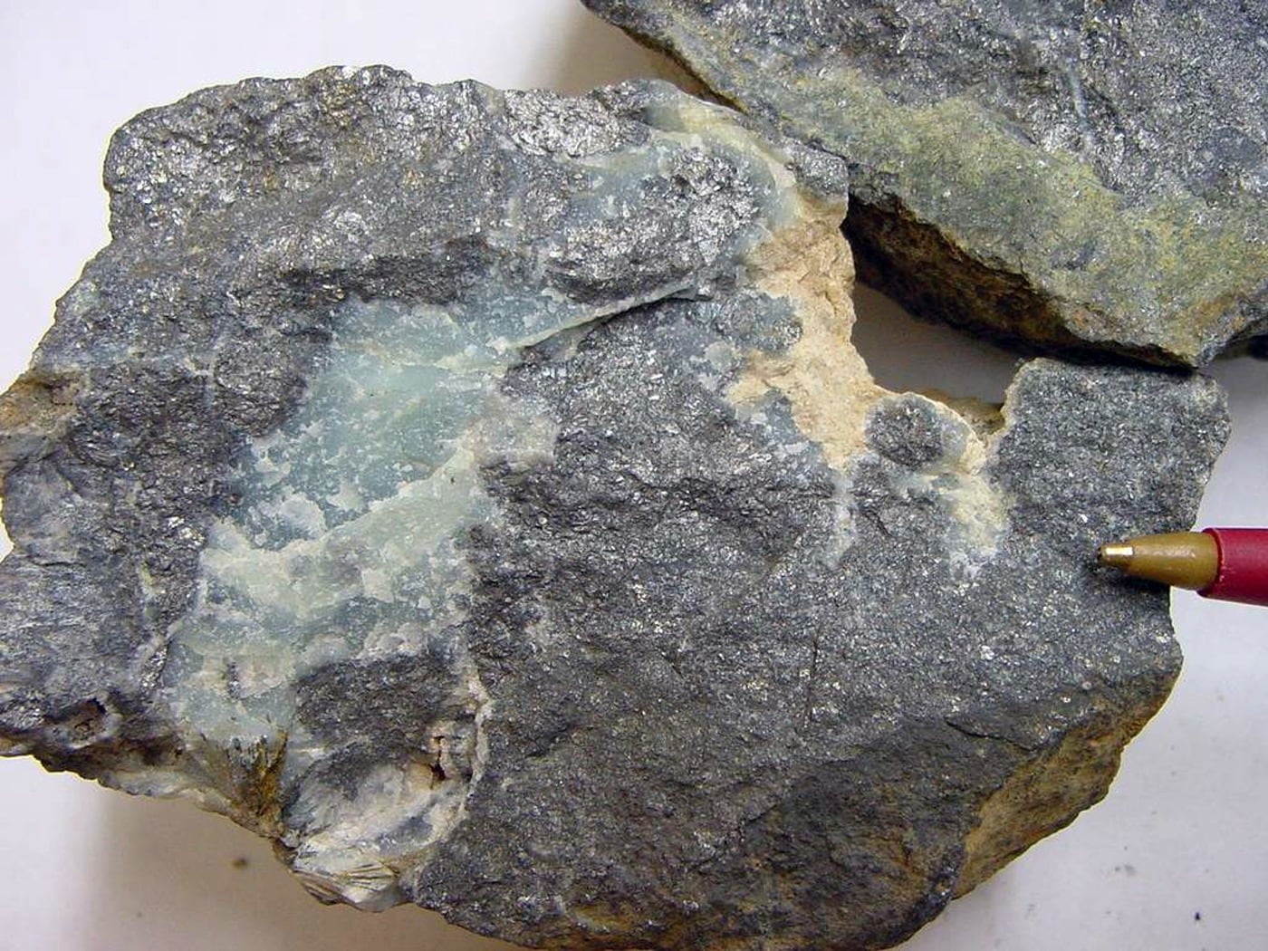 A gray, metallic arsenopyrite mineral specimen, an arsenic-bearing ore, with a pen beside it for scale