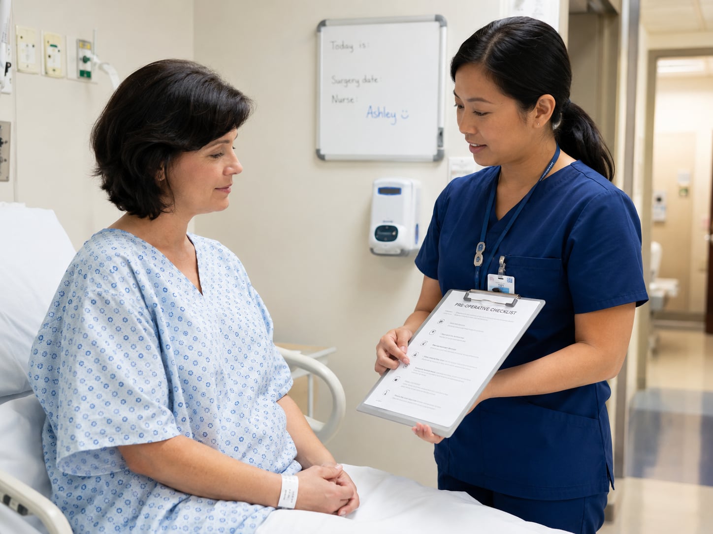 A nurse in navy scrubs holds a clipboard headed “Pre-operative Checklist” while talking with a woman in a hospital gown seated on a bed.
