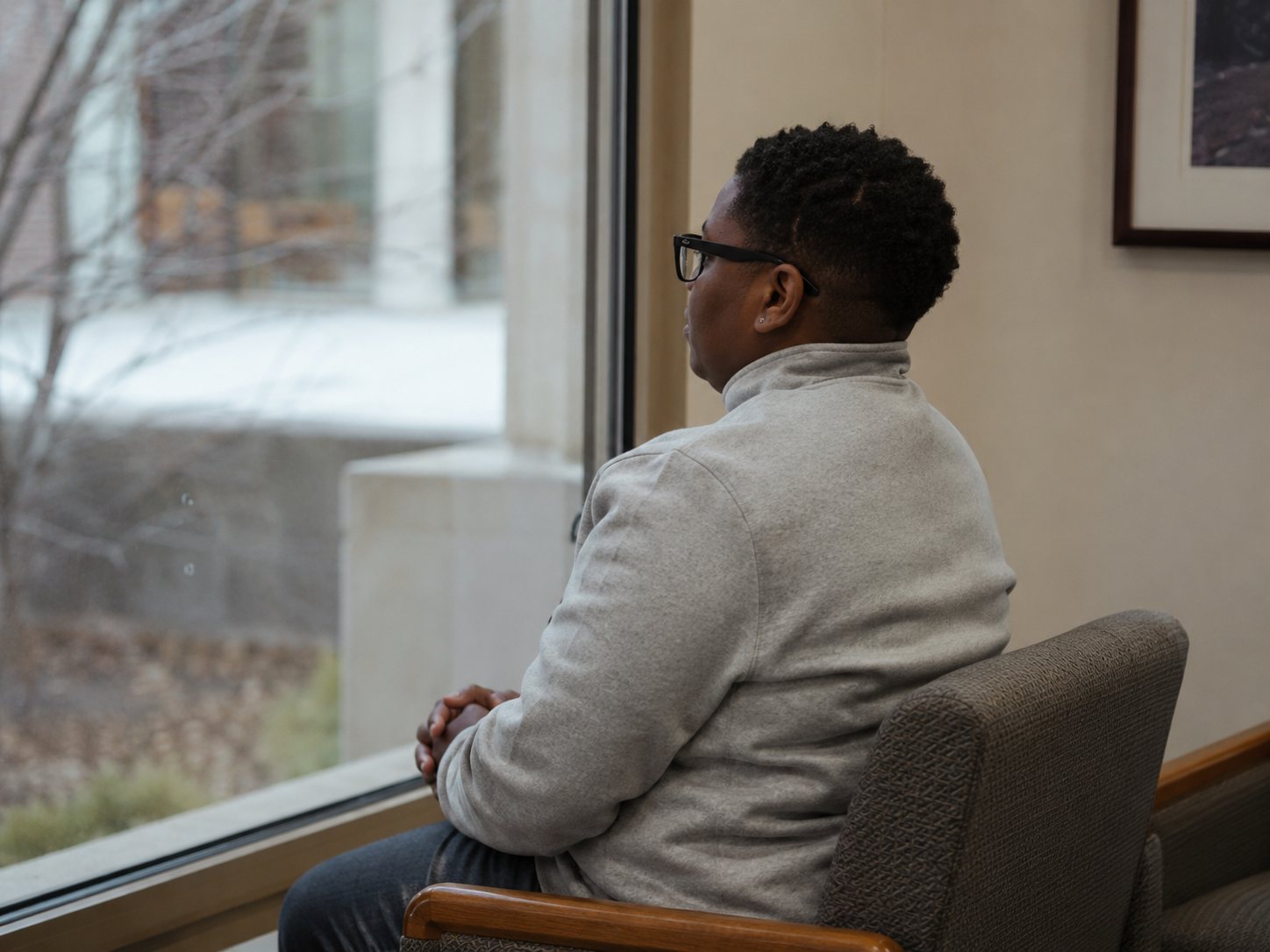 A man sits alone in a hospital armchair looking out of a large window