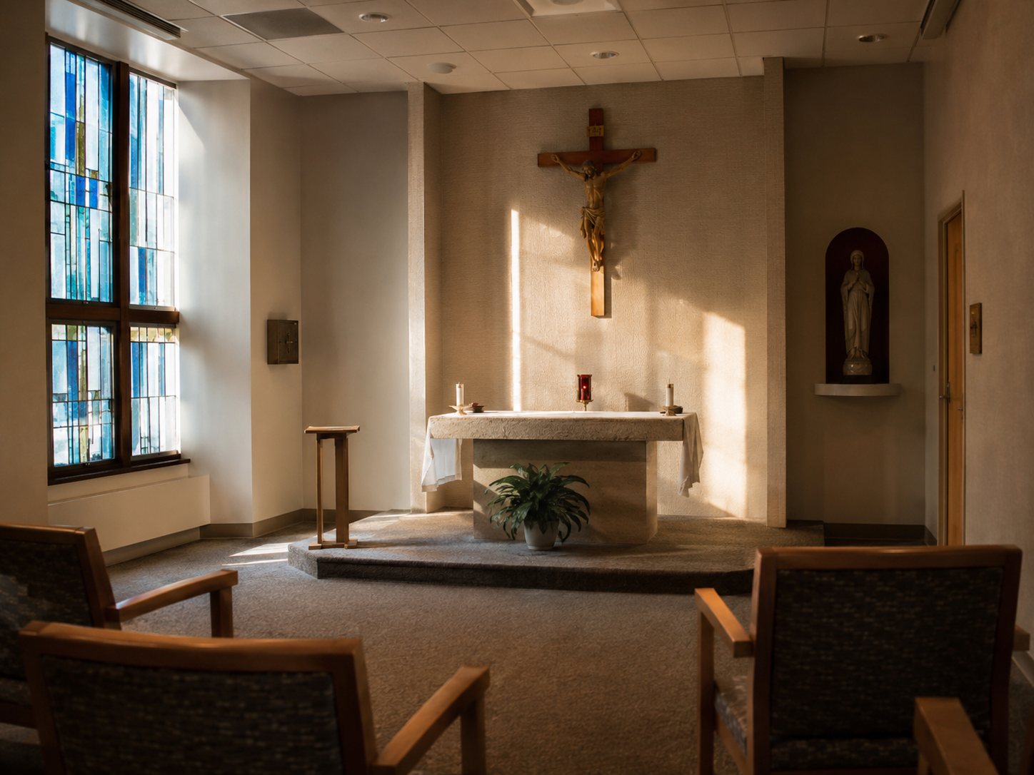 An empty hospital chapel with stained glass, wooden chairs and a stone altar in afternoon light