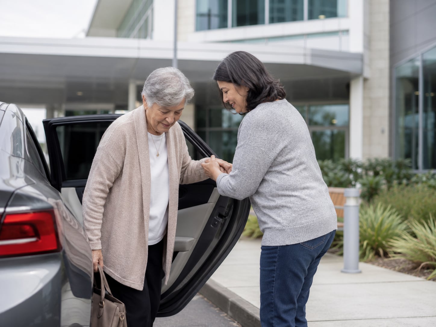 A younger woman helps an older woman out of a car in a driveway