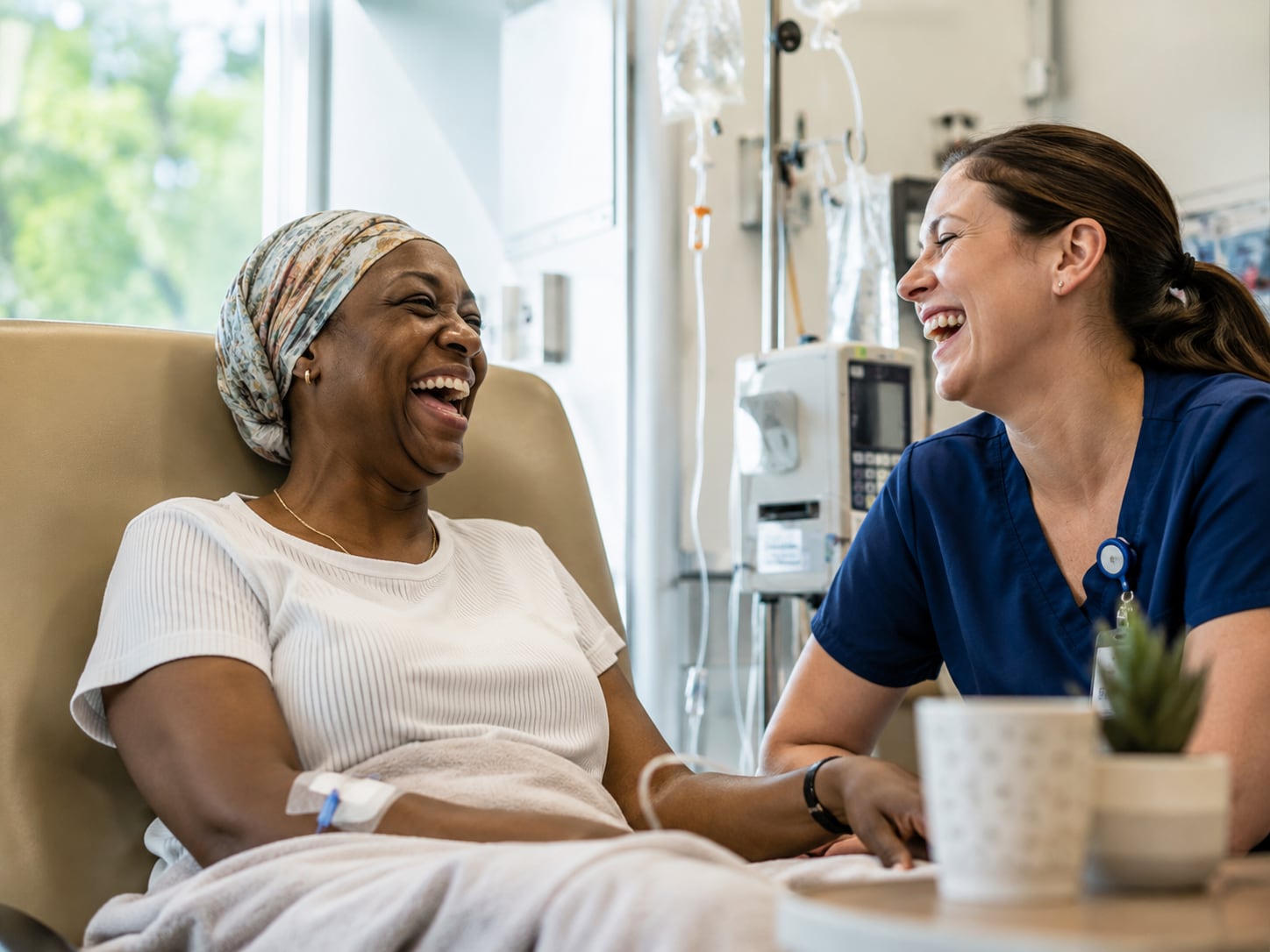 A woman laughs with a nurse during an infusion, IV line visible