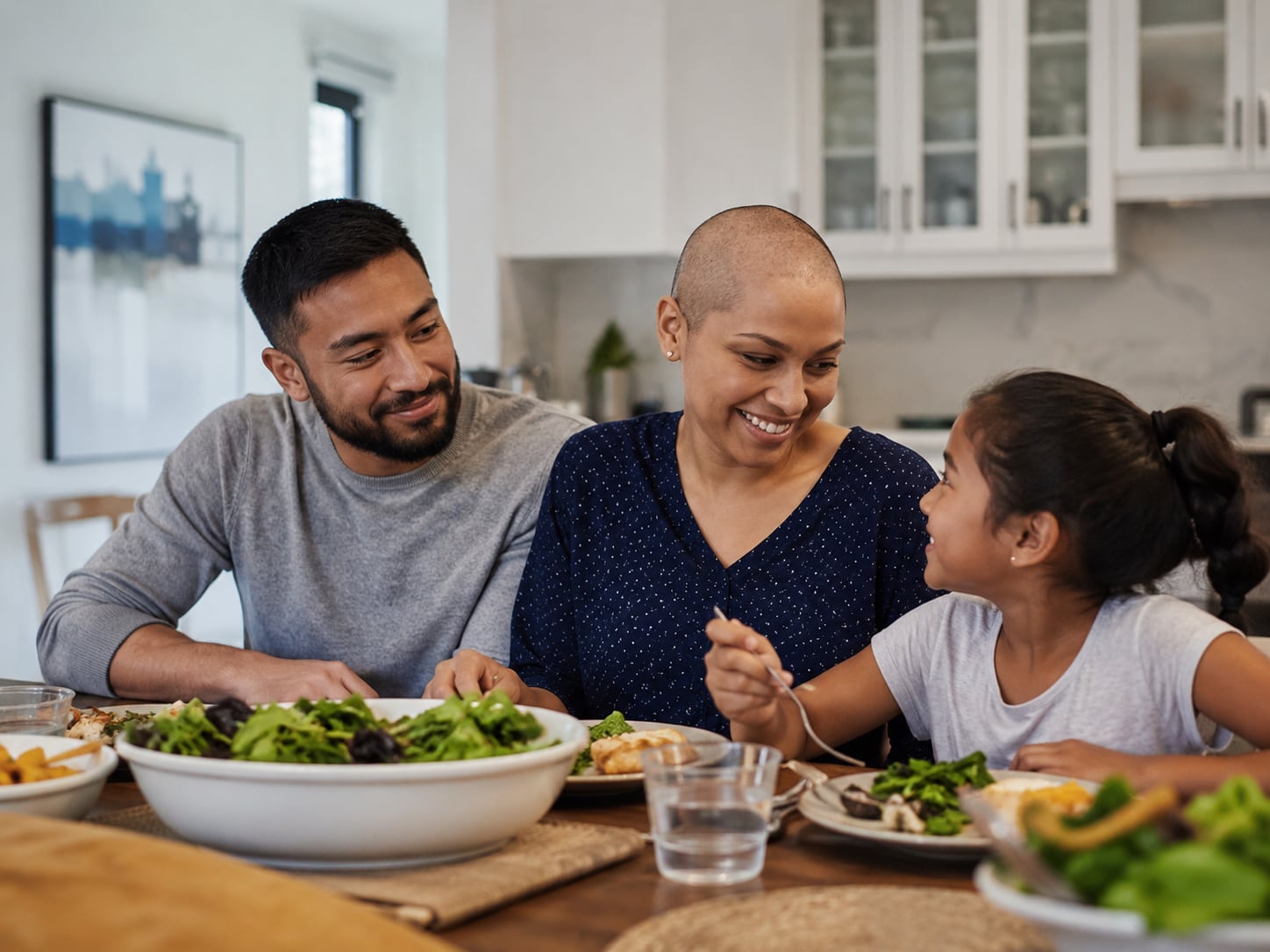 A man, bald woman, and girl laugh together at a dinner table