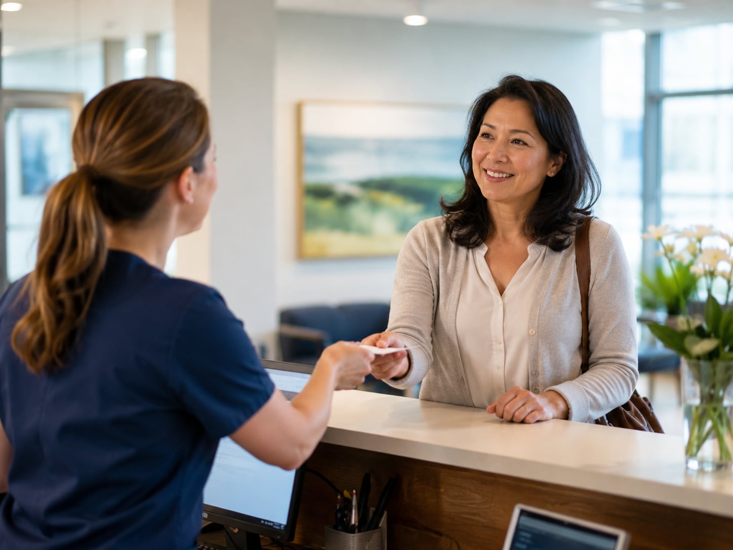 A female clinician smiles while handing something to a woman at a reception counter