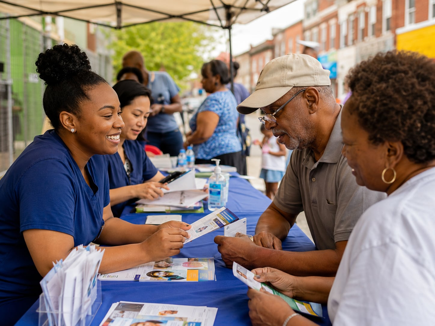 A healthcare workers assist people at an outdoor community health event table