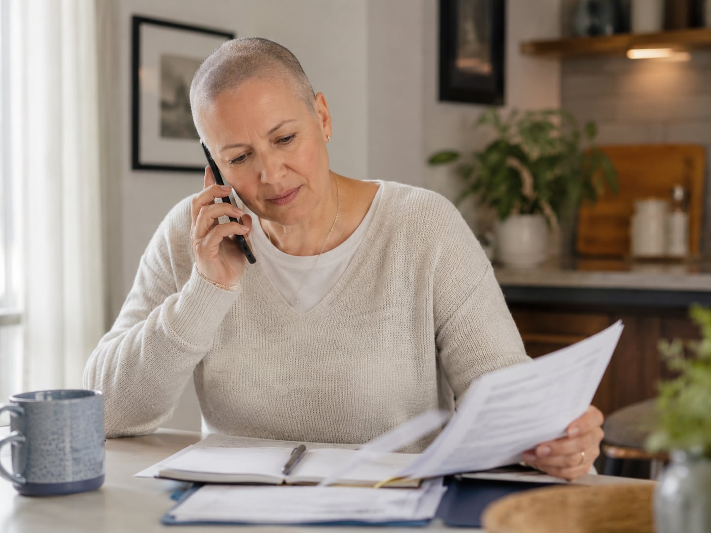 An older woman talks on the phone while holding a paper at home