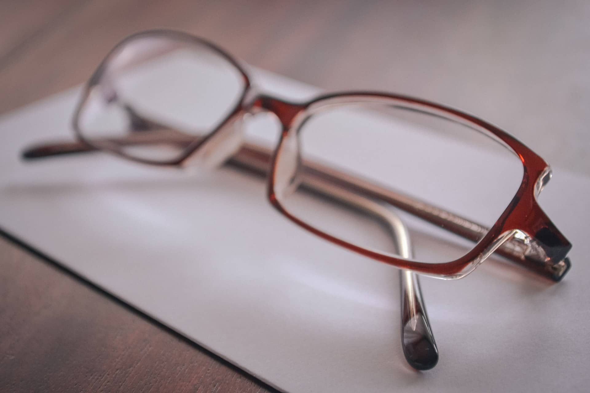 A pair of reddish-brown eyeglasses lying on a sheet of paper.