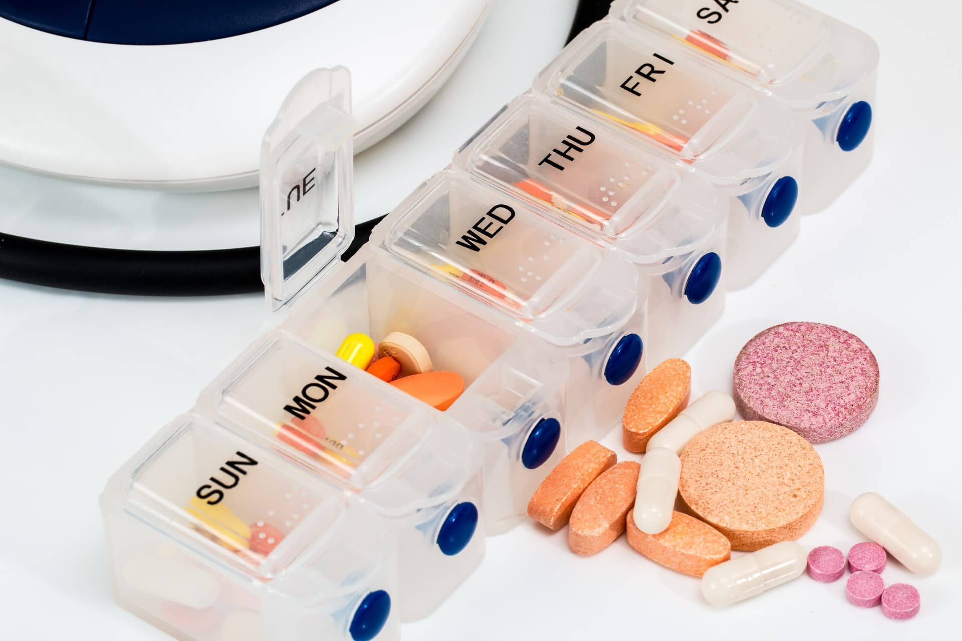 A clear weekly pill organizer with tablets and capsules beside it.