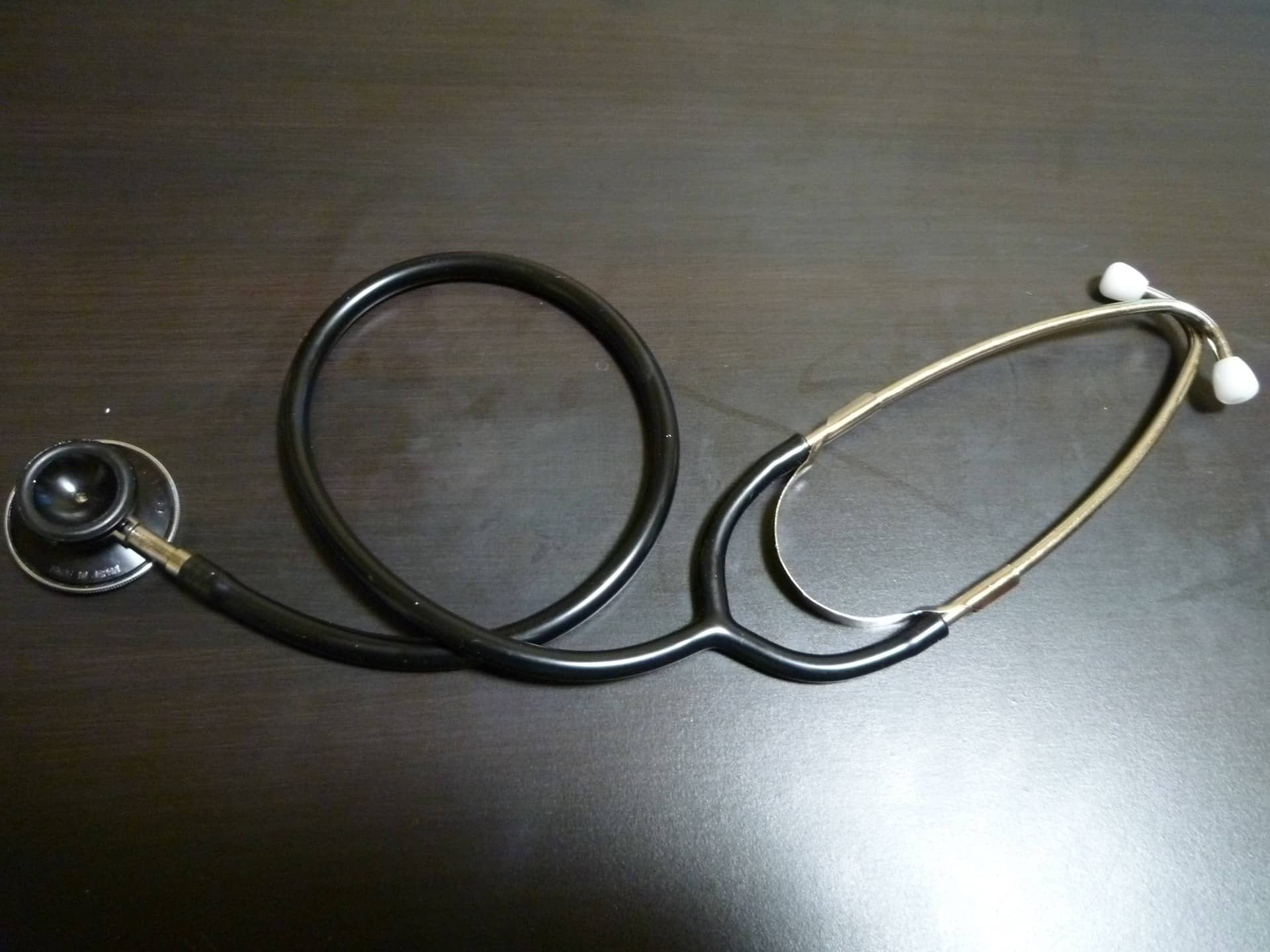 A stethoscope lying coiled on a dark wooden table.