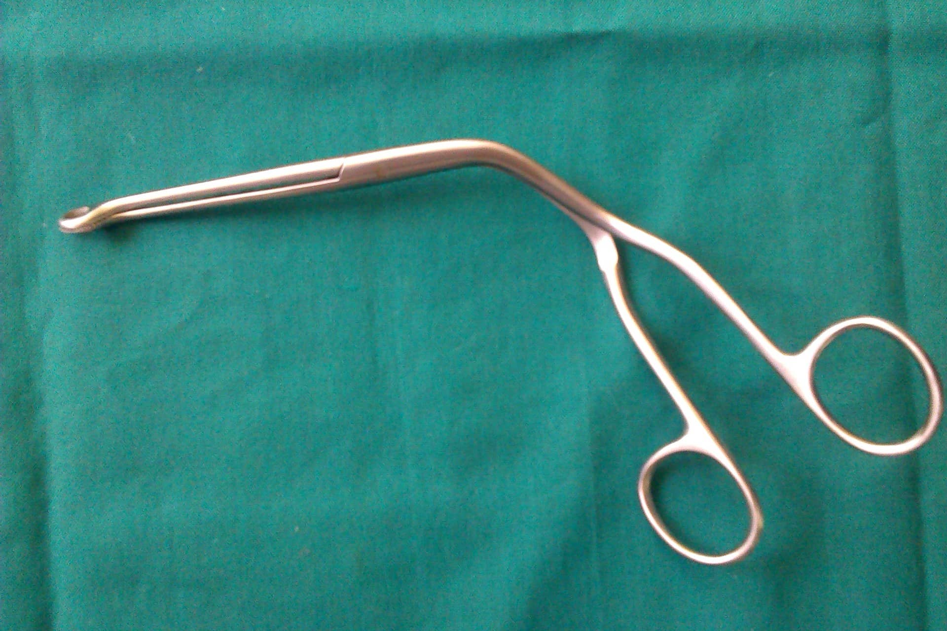 A metal surgical instrument with two finger rings lying on a green cloth.