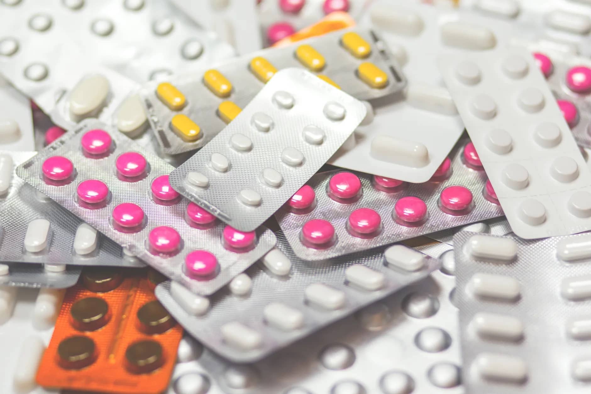 A heap of silver foil blister packs holding pink, yellow and white tablets.