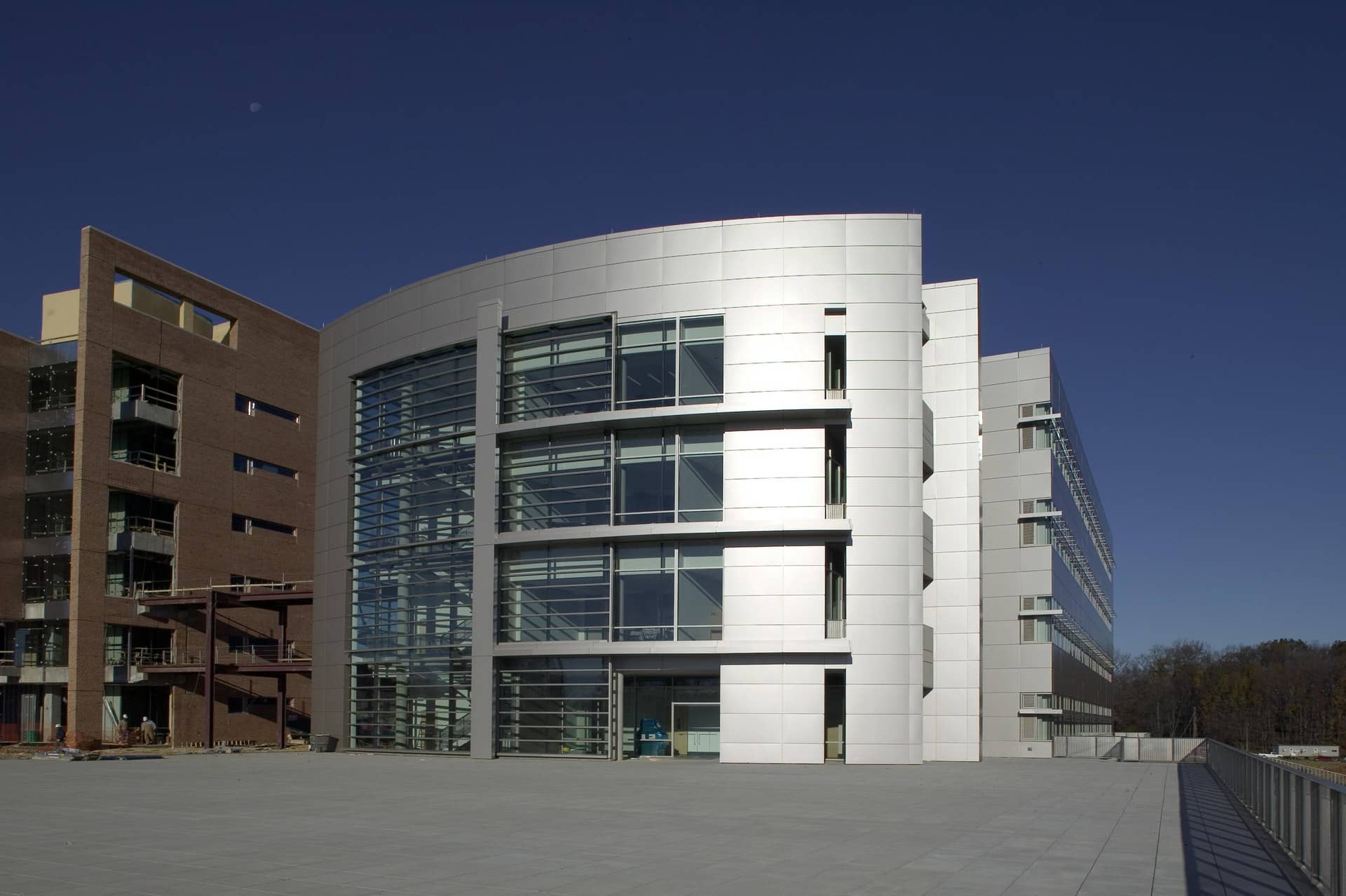 A curved silver metal-and-glass building beside a brick building under a deep blue sky.