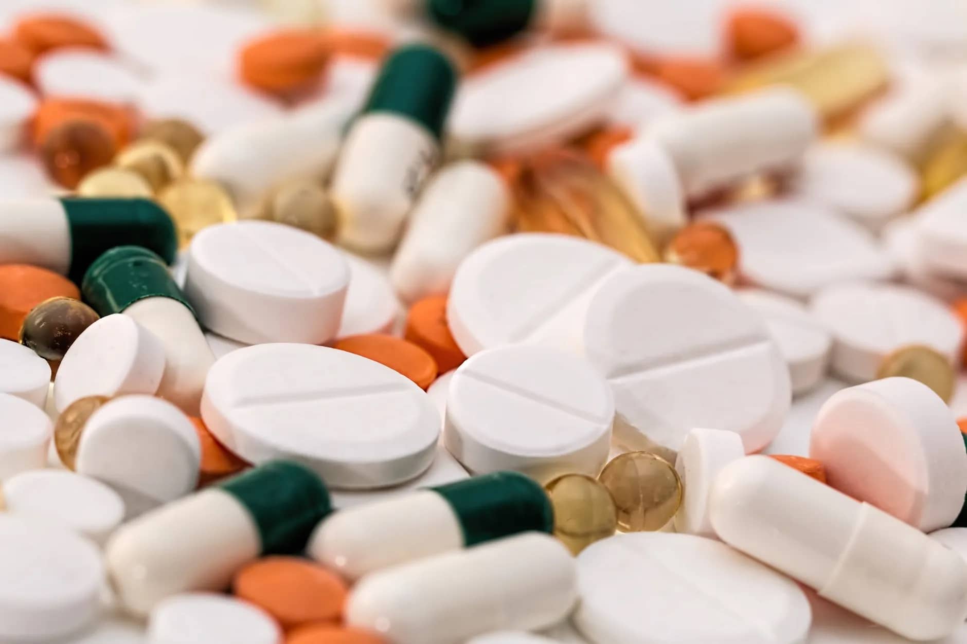 Close view of many white tablets, green-and-white capsules and orange pills heaped together.