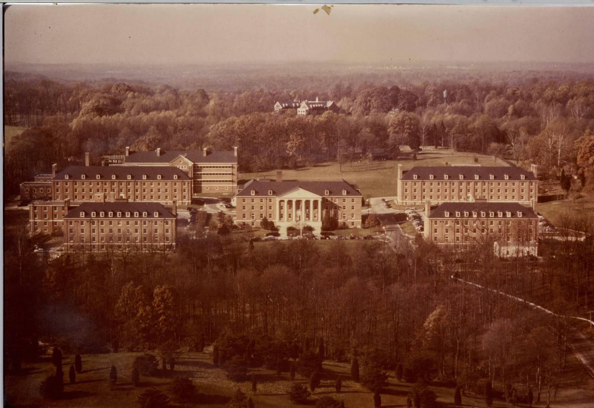 Faded color aerial photograph of brick buildings among autumn trees on a campus.