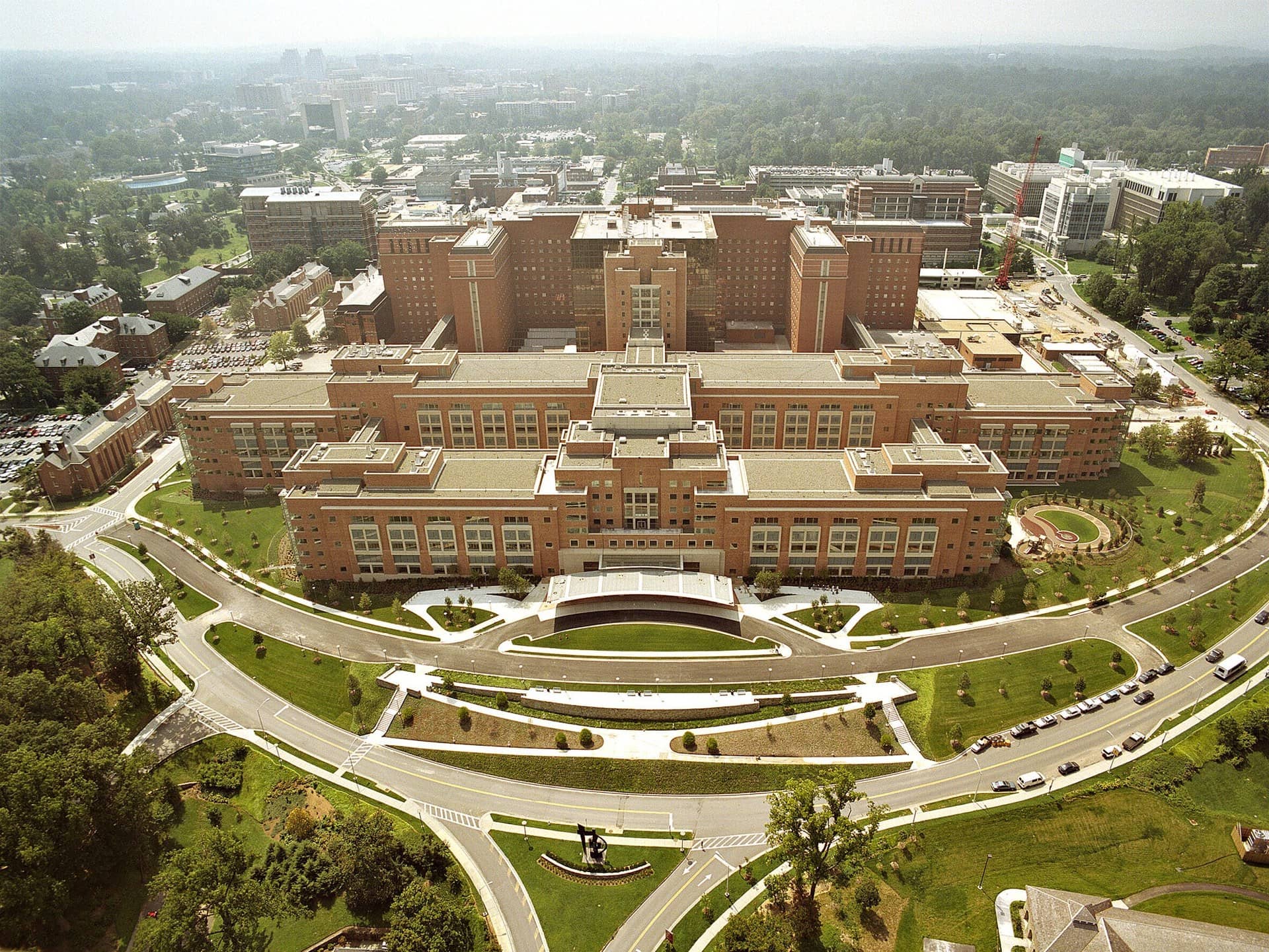 Aerial view of a large brick hospital and research complex with curving roads and lawns.