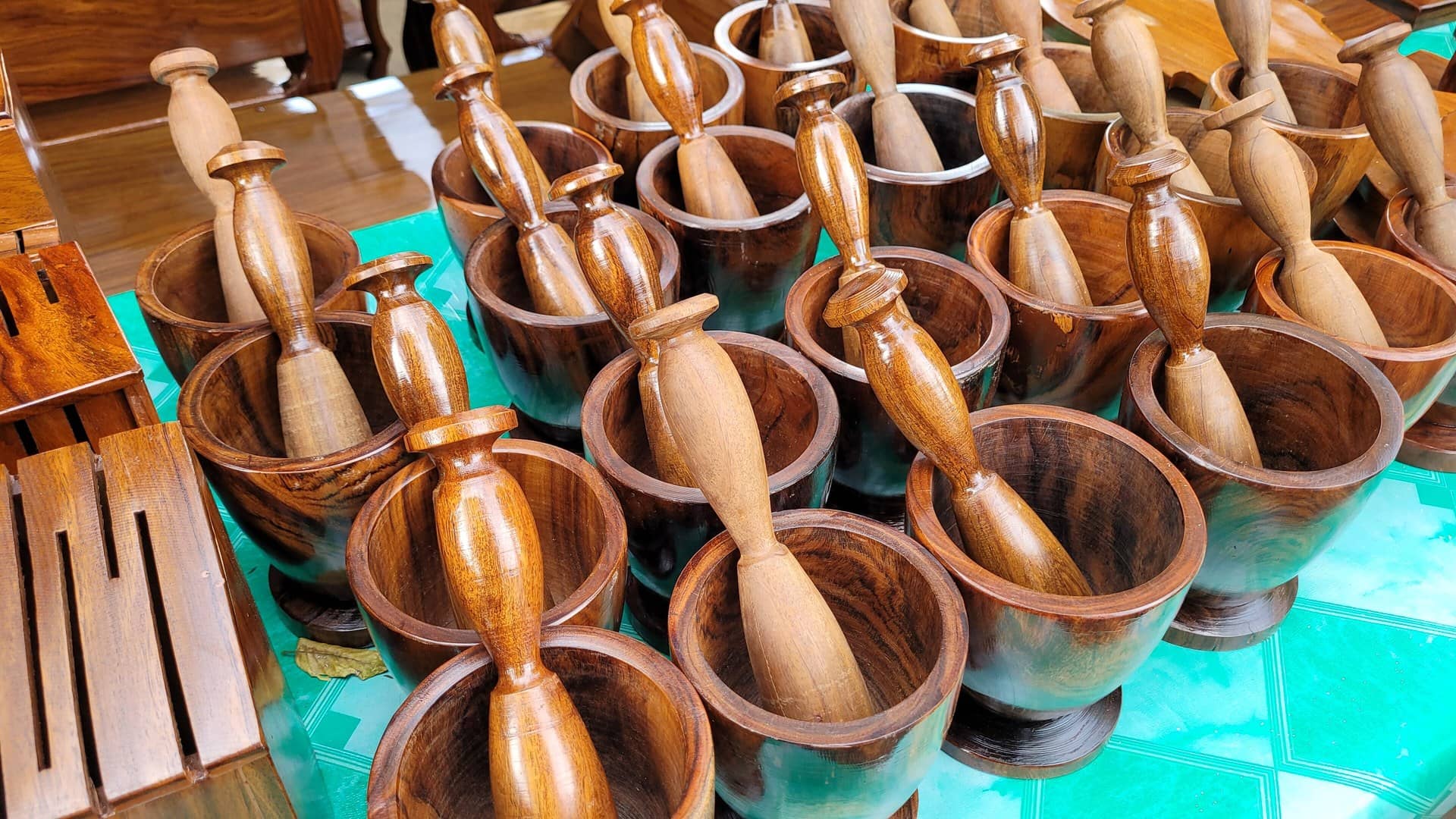 Many dark wooden mortars each holding a wooden pestle on a green table.
