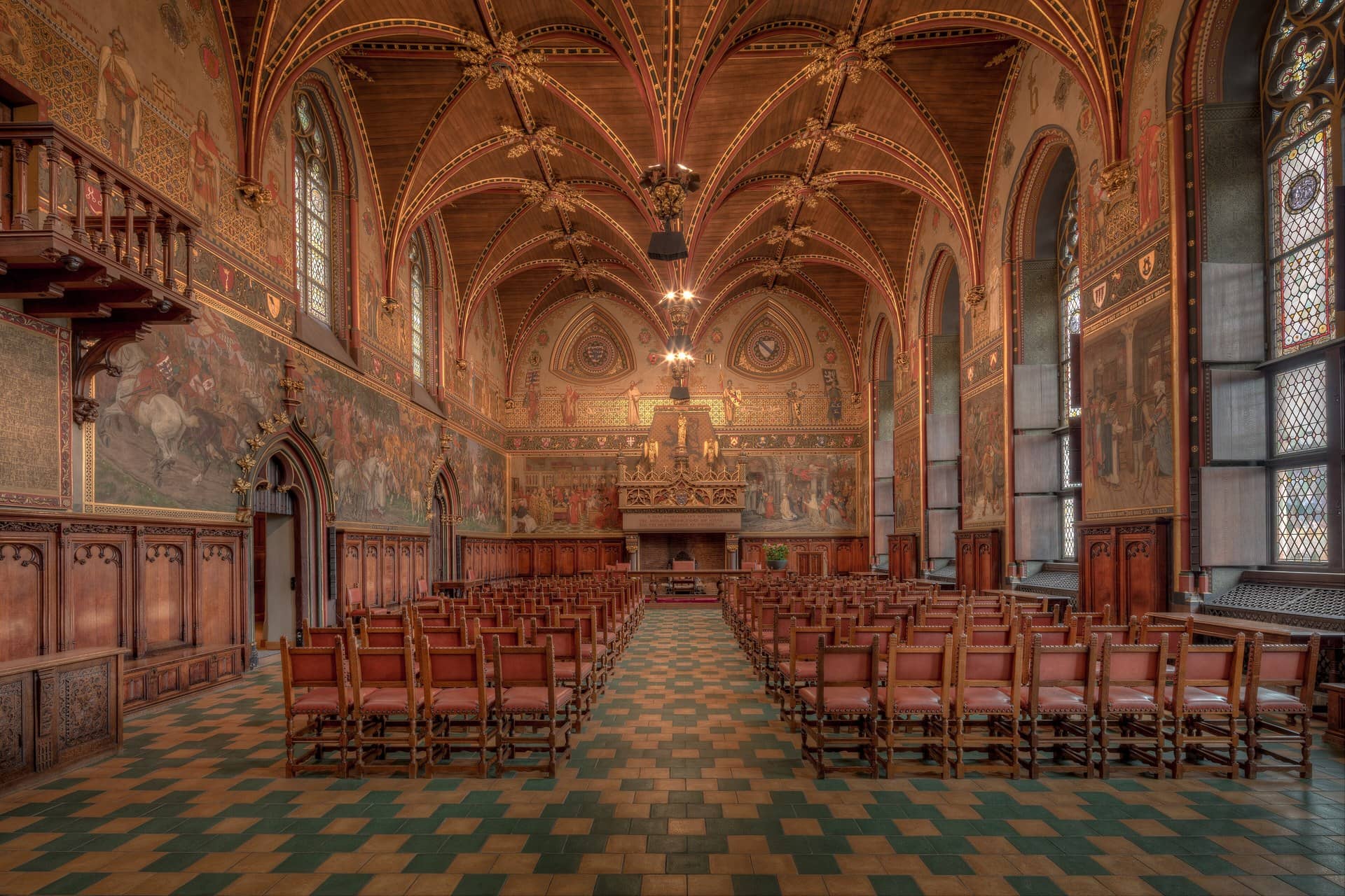 Empty ornate hall with rows of chairs, painted walls and a vaulted wooden ceiling.