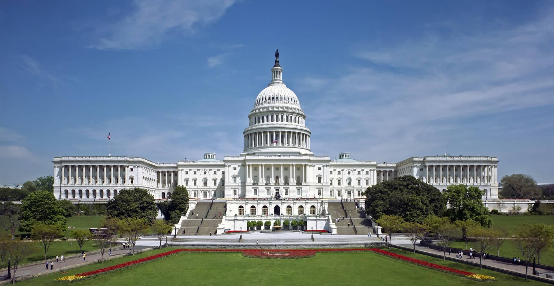 A large white domed legislative building and its lawn and flower beds on a clear day.