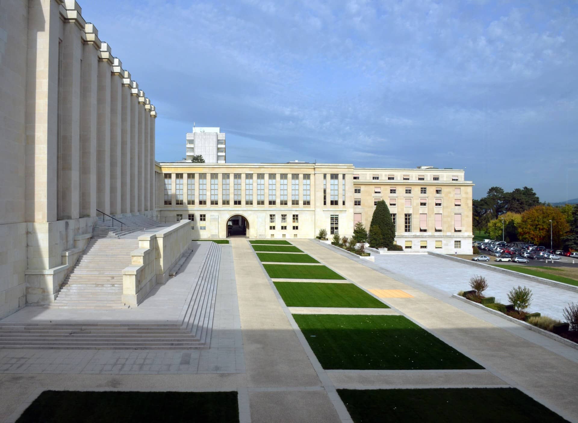 Large stone buildings with steps and lawns in a courtyard under a blue sky.