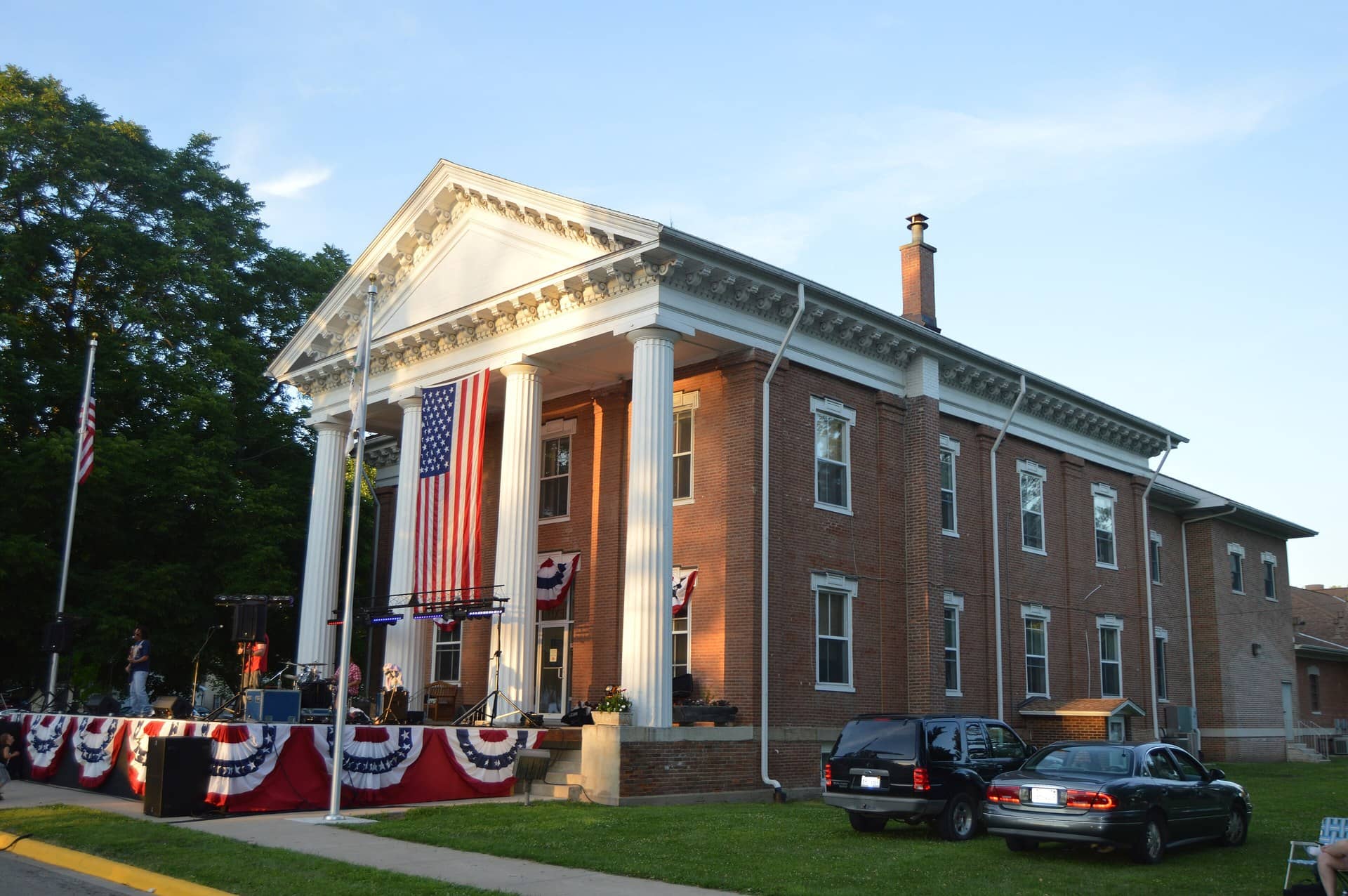 Brick courthouse with white columns, a large American flag and red-white-blue bunting.