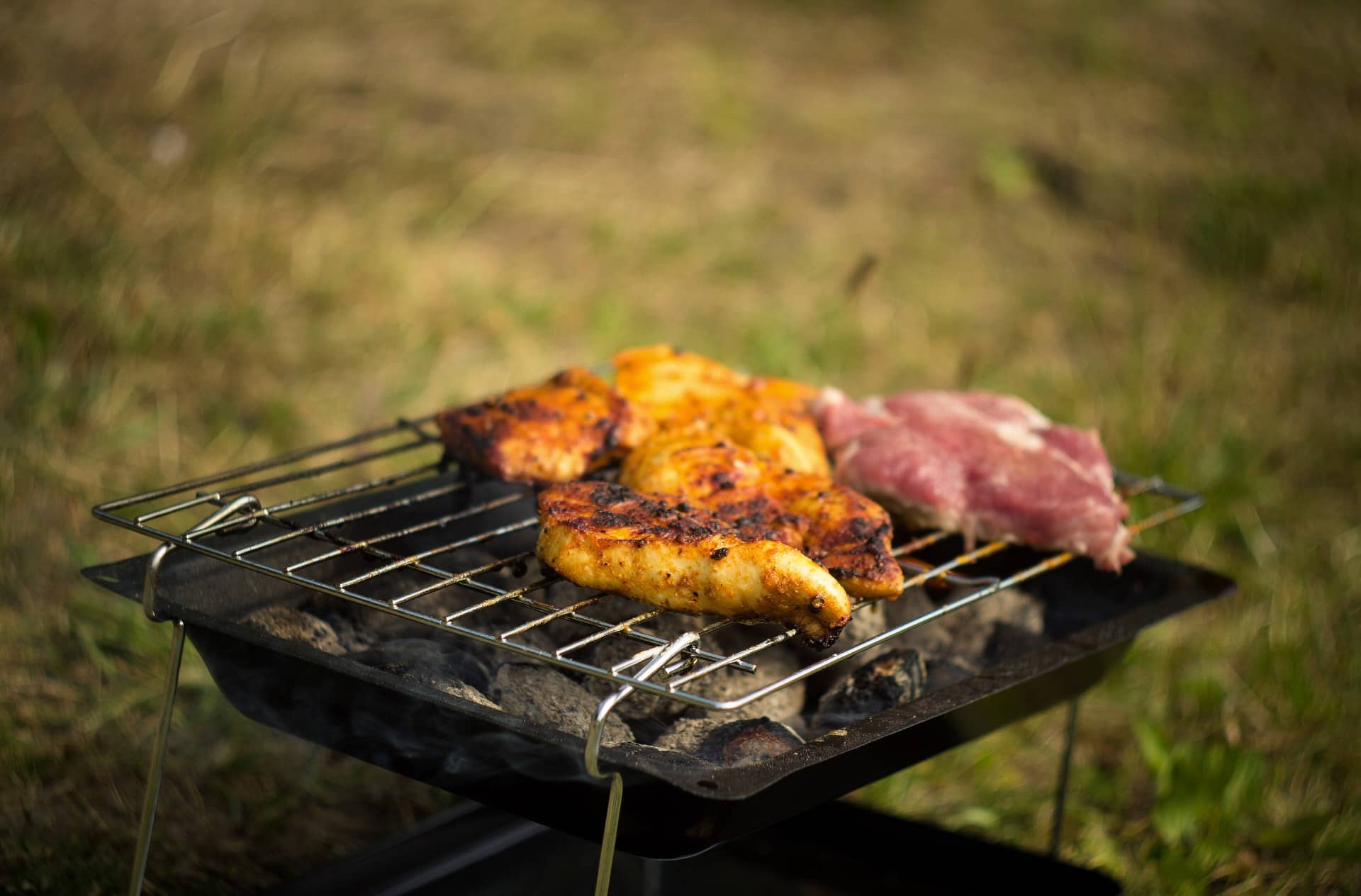 Pieces of chicken and other meat grilling over charcoal on a small outdoor grill.