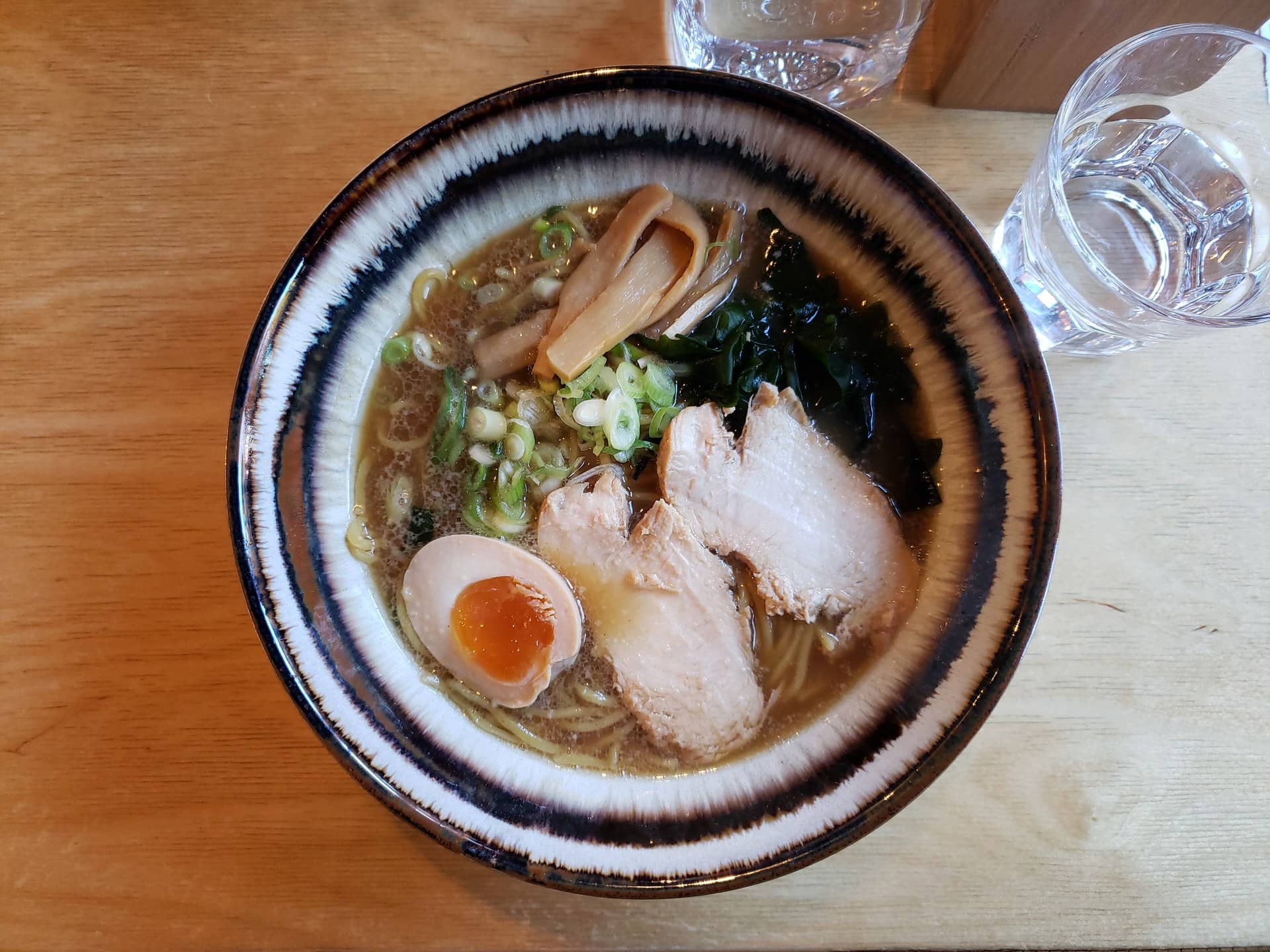 A bowl of noodle soup with sliced meat, egg and seaweed, beside a glass of water.