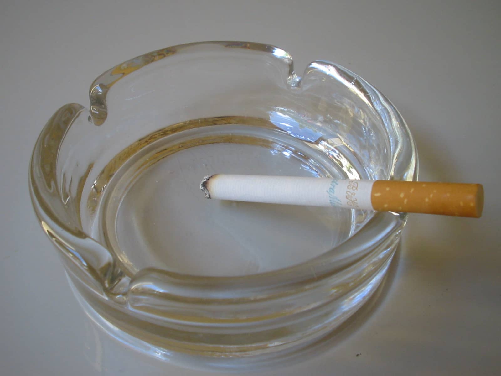 A cigarette resting in a clear glass ashtray.