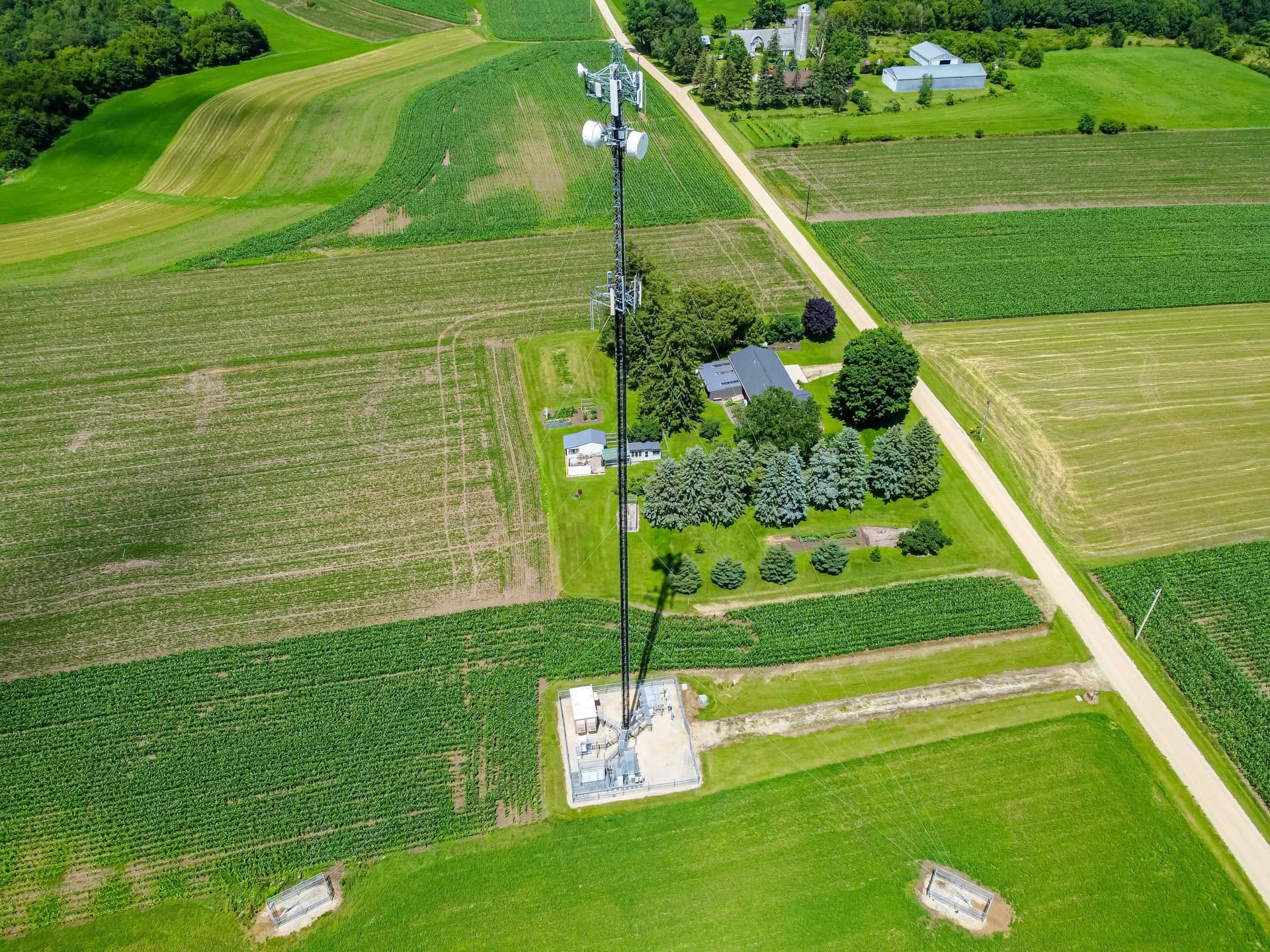 Aerial view of a tall cell-phone tower among green crop fields and a farmstead.
