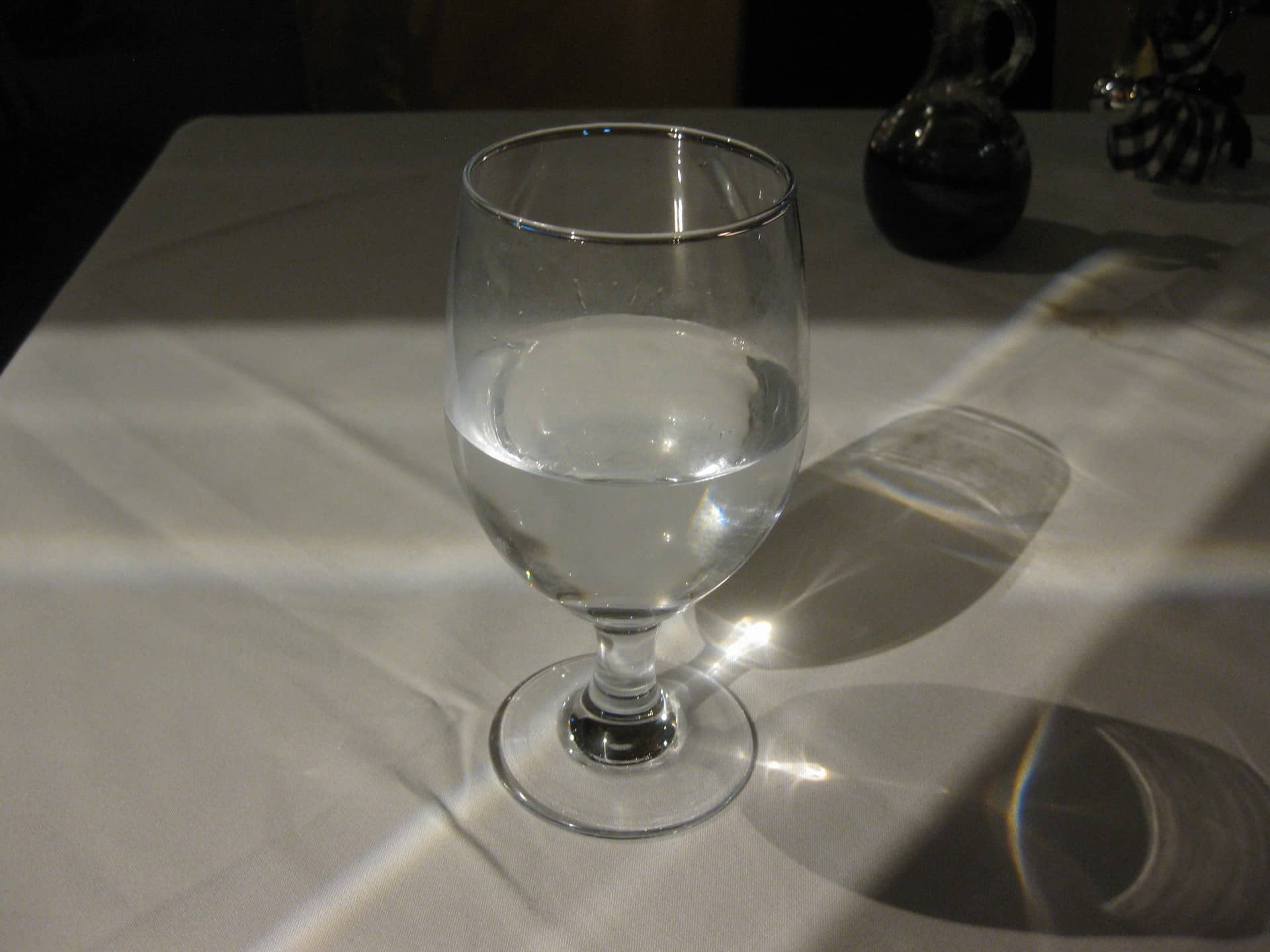 A stemmed glass of clear water on a cloth-covered table with light and shadow.