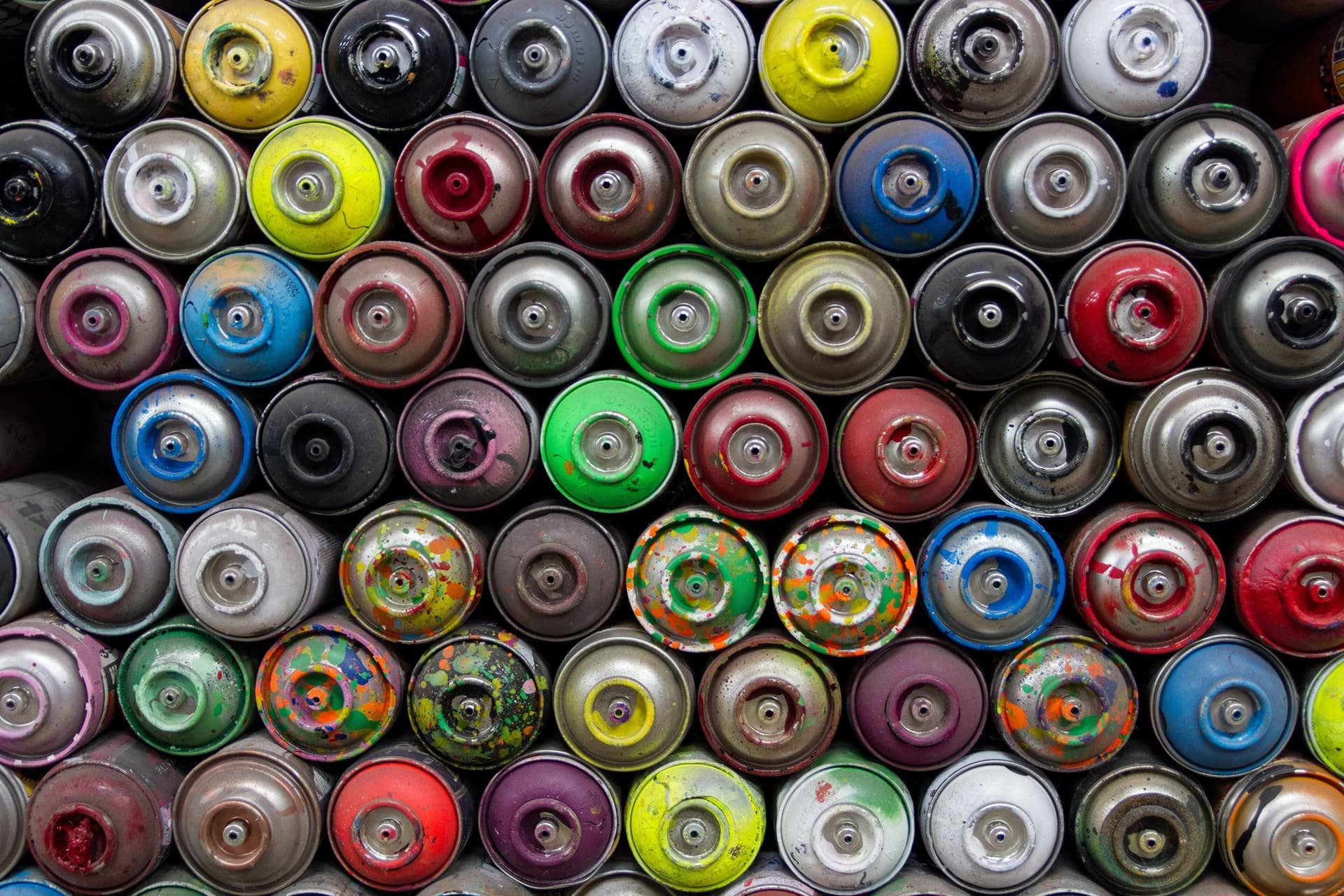 A dense grid of used spray-paint cans viewed end-on in many colours.