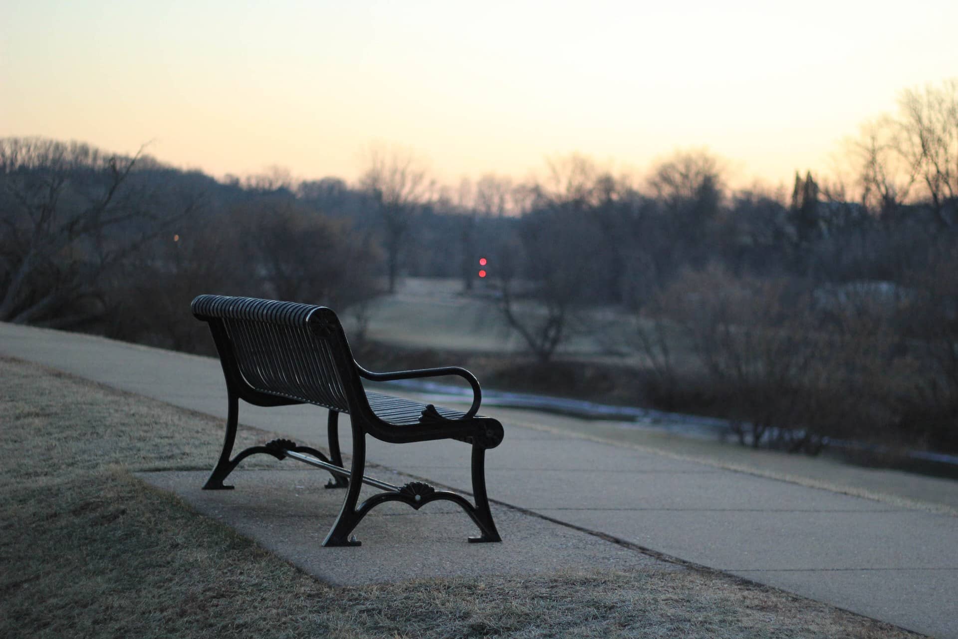 An empty dark metal park bench beside a path at dusk.