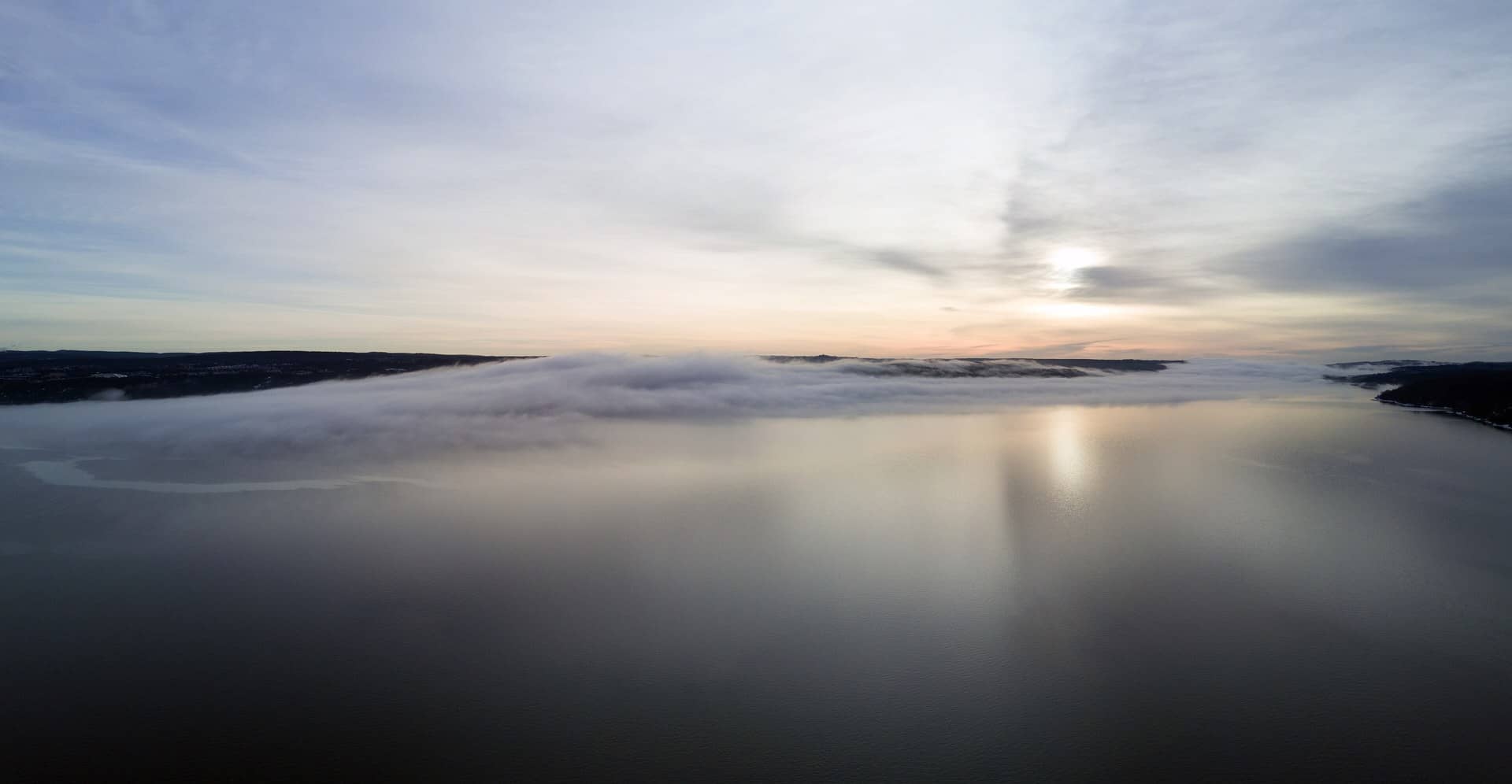 Low fog over calm water under a pale sky.