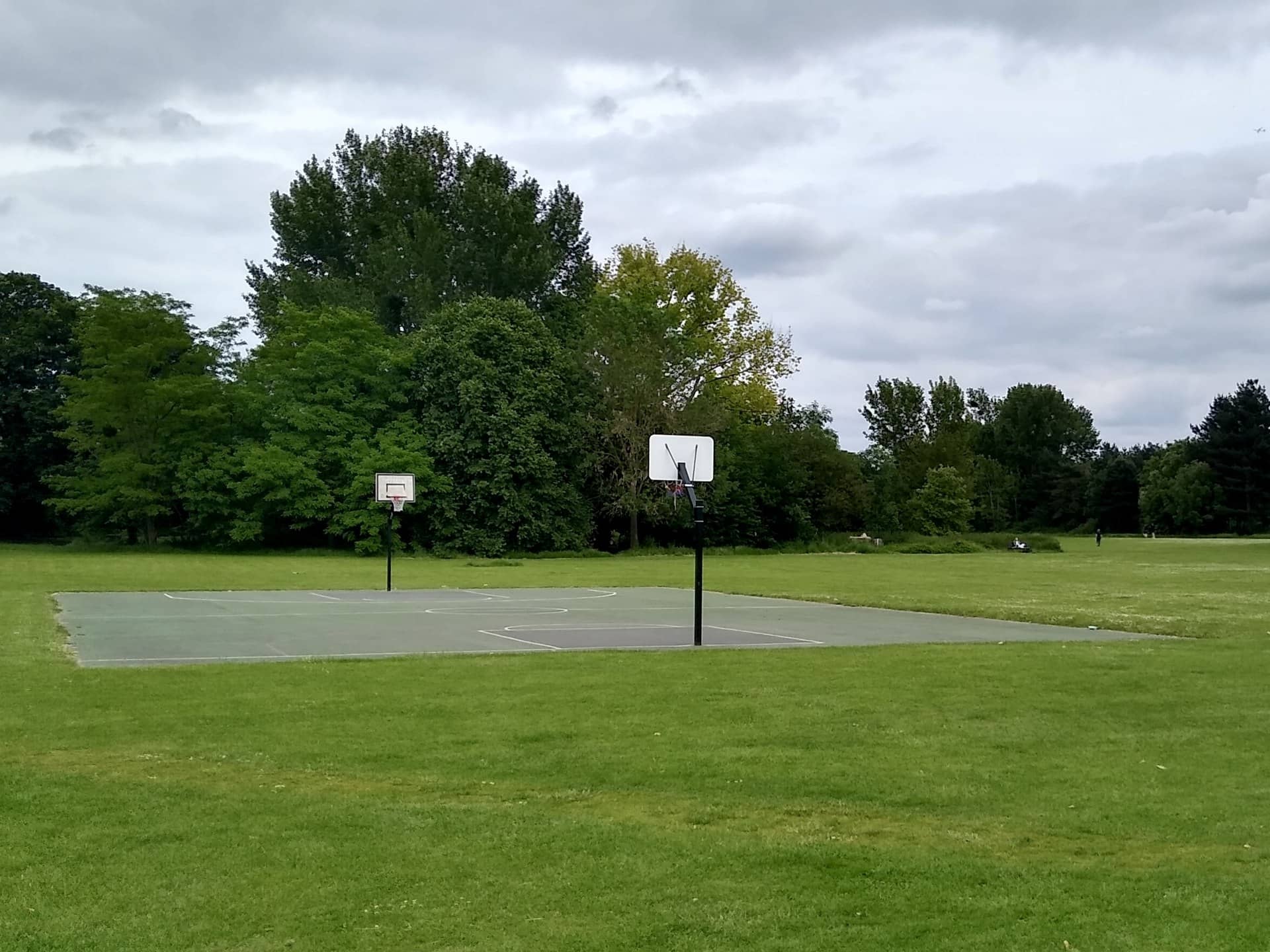 An empty outdoor basketball court with two hoops on a grassy park.