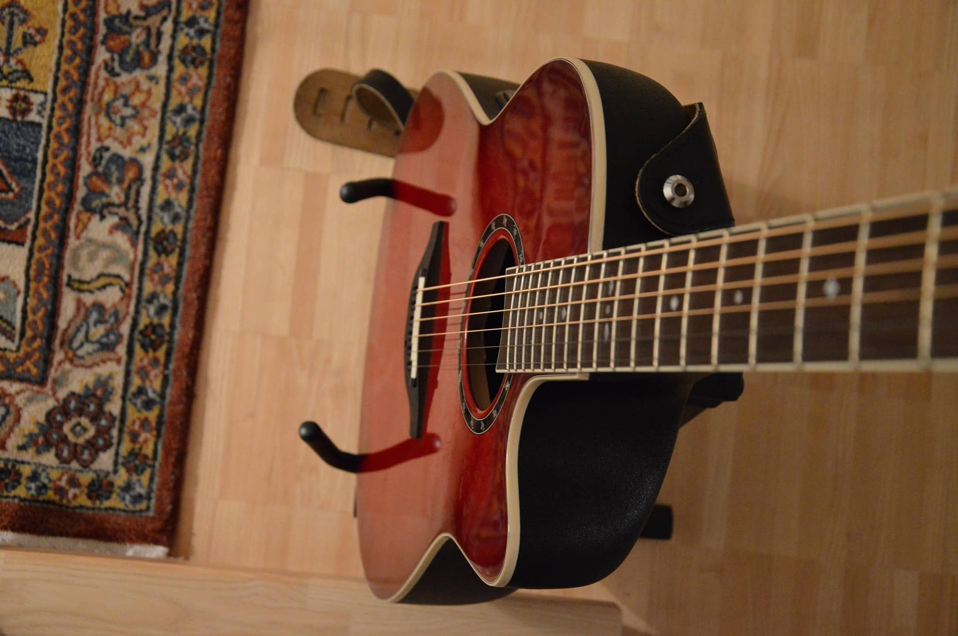 A red acoustic guitar held on a stand beside a patterned rug.