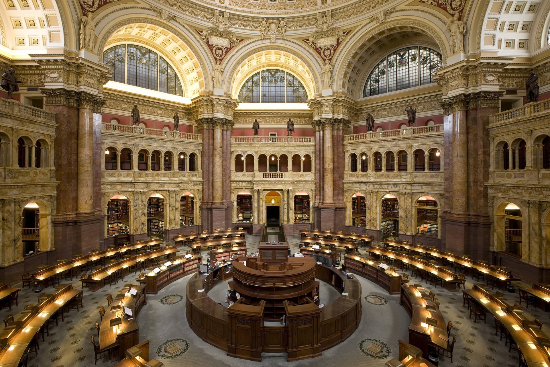 A grand domed library reading room with curved wooden desks and few people.