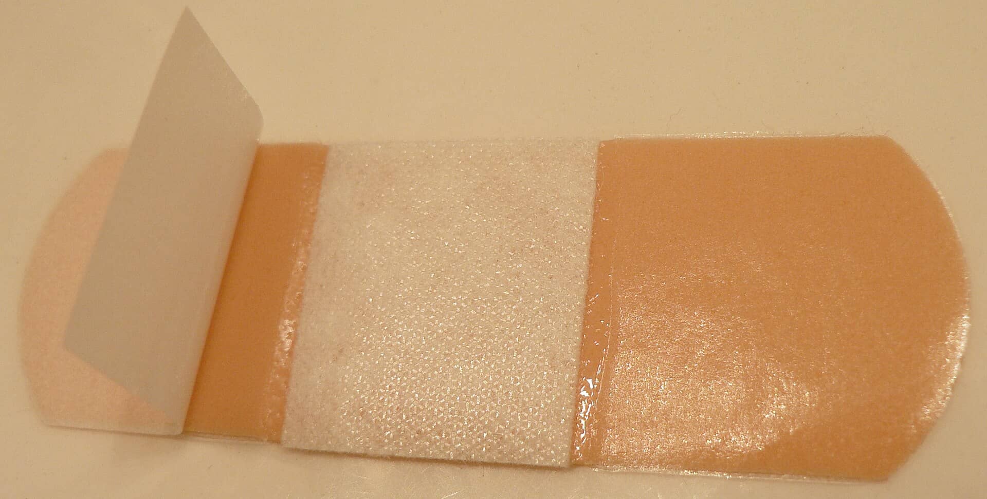 A close-up of an adhesive bandage with its paper backing partly peeled back.