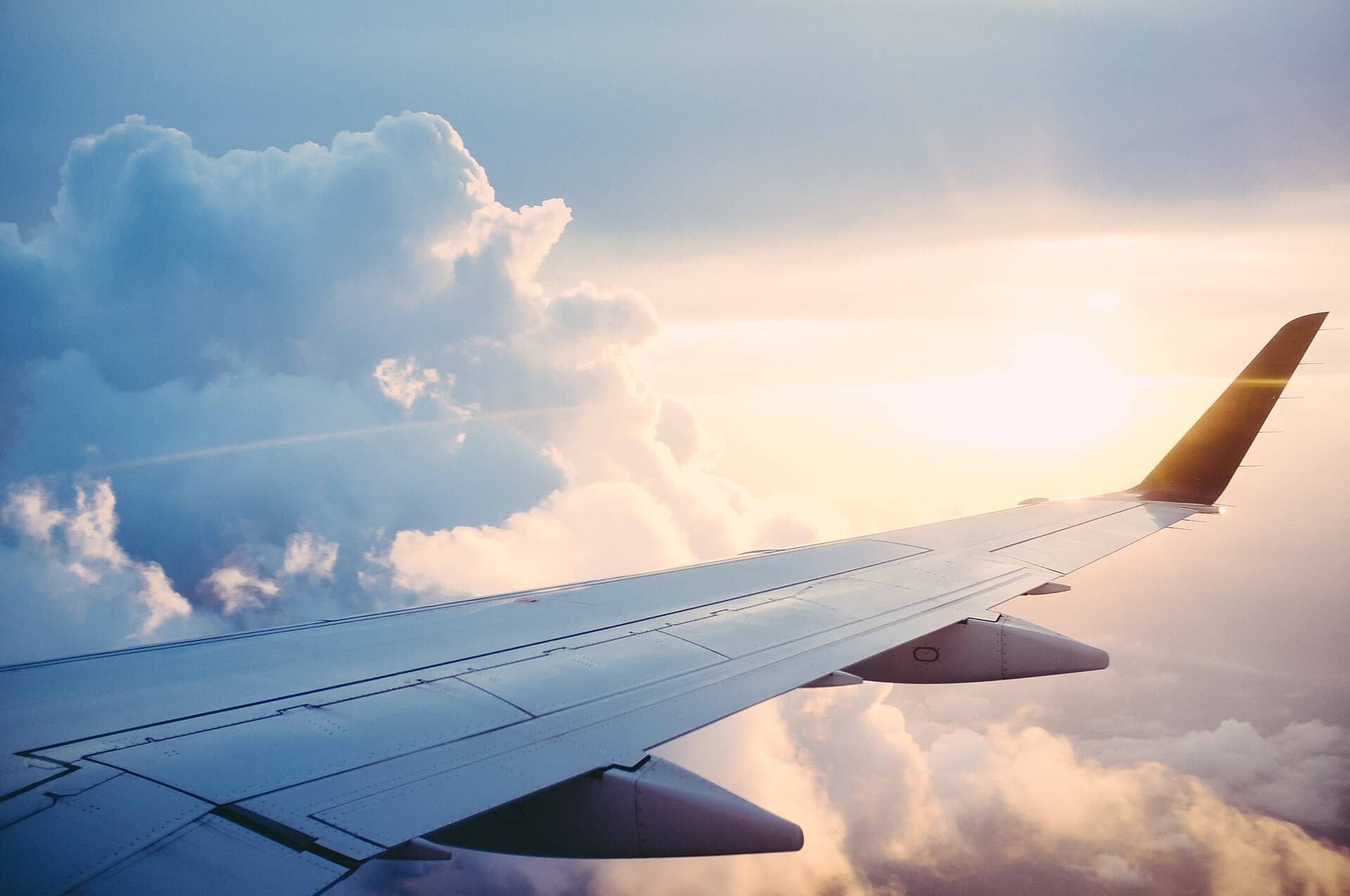 An airliner wing and winglet seen from a window above clouds in warm low sunlight.