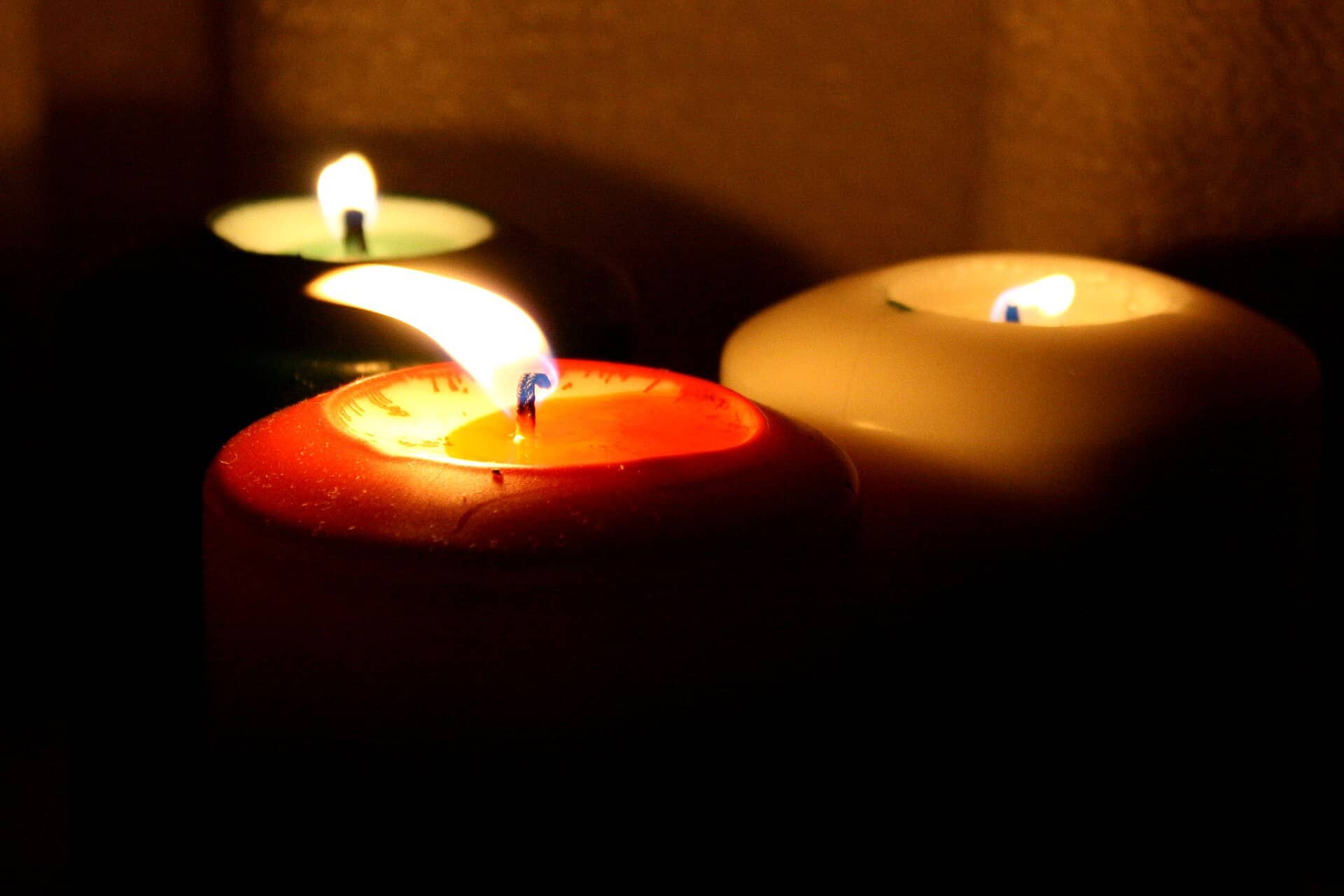 Three lit candles, red, white and dark green, glowing in a dim room.