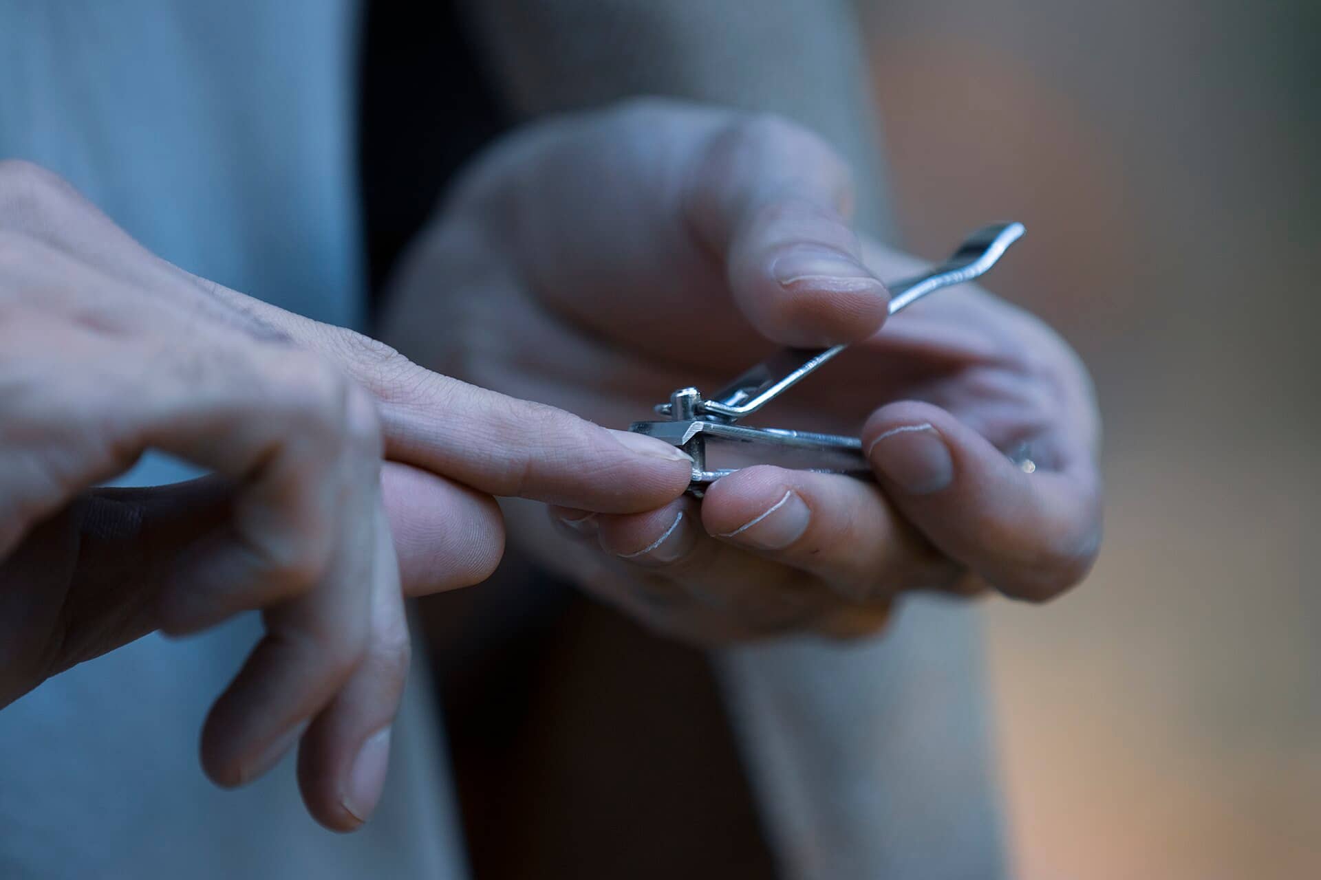 Close view of a person's hands using a metal nail clipper on a fingernail.