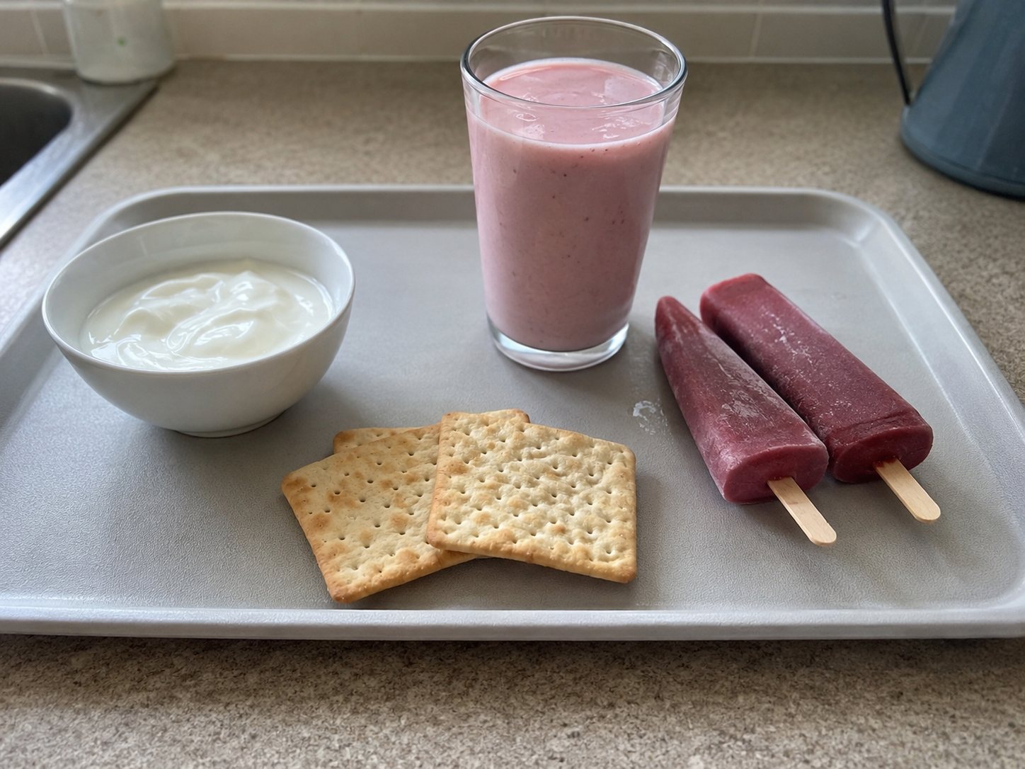 A tray holding plain yoghurt, saltine crackers, a pink smoothie and two fruit ice lollies