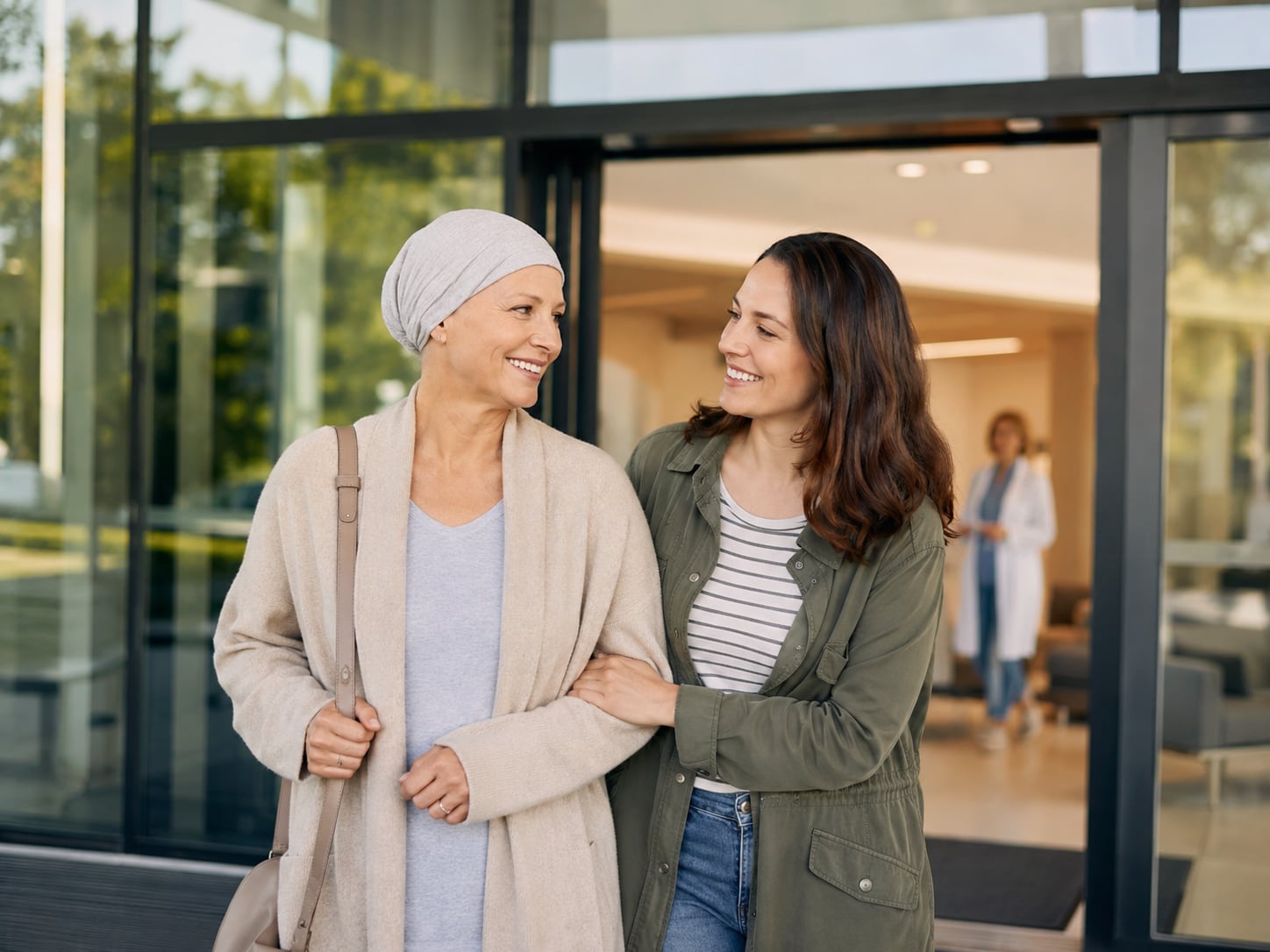 A woman with a headscarf walks smiling alongside another woman in a glass-walled hallway