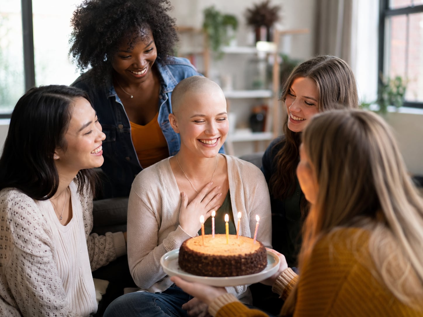 A group of women celebrate with a cake around a woman with a headscarf